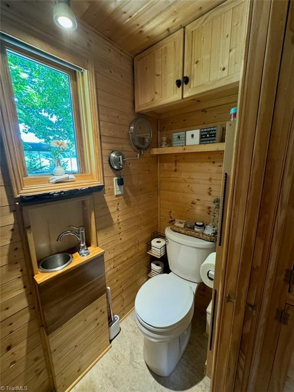 bathroom featuring toilet, wooden walls, and wood ceiling