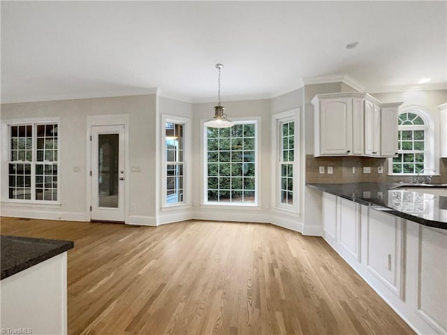 kitchen featuring white cabinetry, dark stone countertops, hanging light fixtures, and light hardwood / wood-style flooring