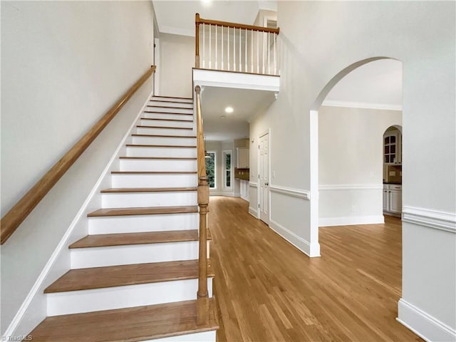 stairway featuring a high ceiling, ornamental molding, and wood-type flooring