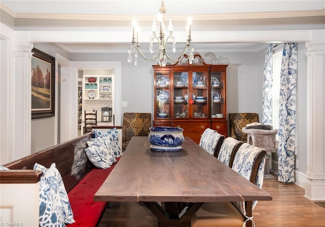 dining room with a notable chandelier, hardwood / wood-style flooring, ornamental molding, and ornate columns