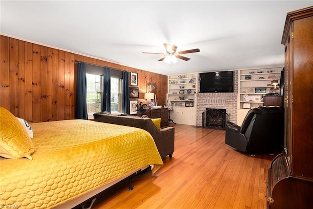 bedroom featuring ceiling fan, wooden walls, light wood-type flooring, and a fireplace