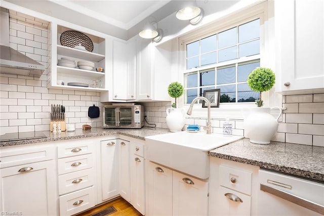 kitchen featuring light stone counters, sink, tasteful backsplash, wall chimney exhaust hood, and white cabinetry