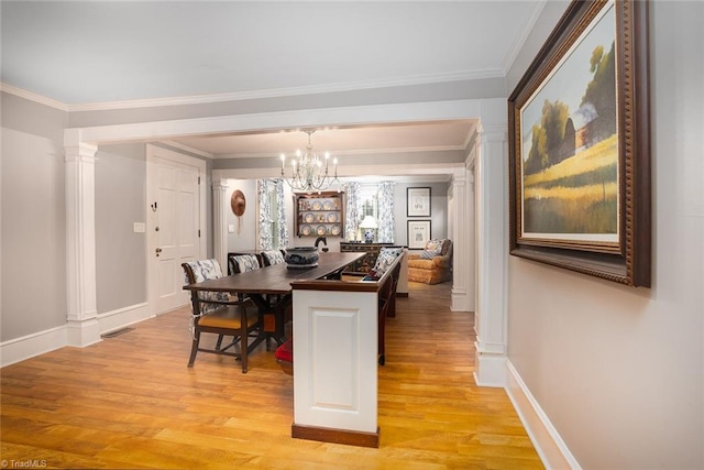 dining space featuring light wood-type flooring, crown molding, a notable chandelier, and ornate columns