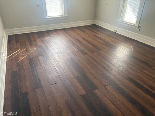 spare room with dark wood-type flooring, plenty of natural light, and baseboards