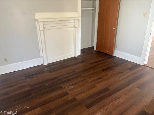 unfurnished bedroom featuring baseboards, dark wood finished floors, and a closet