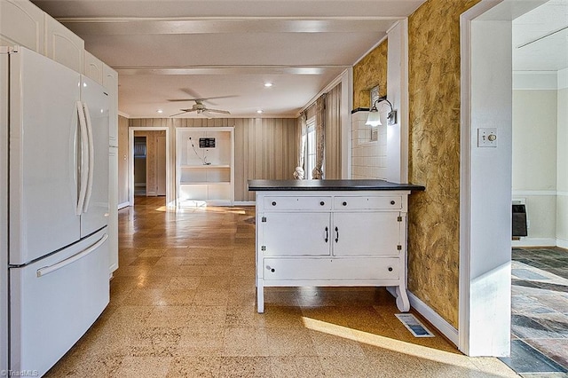 kitchen featuring ornamental molding, ceiling fan, white cabinets, white fridge, and wood walls