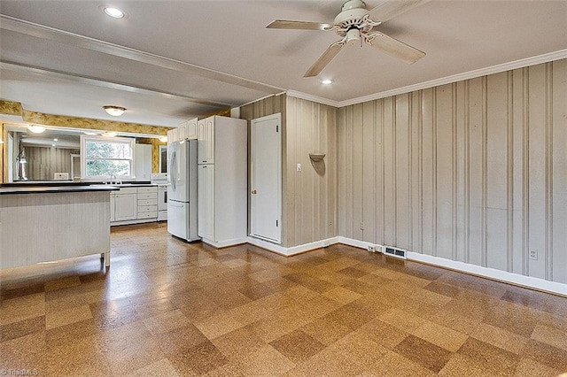 interior space with ceiling fan, wood walls, ornamental molding, and sink