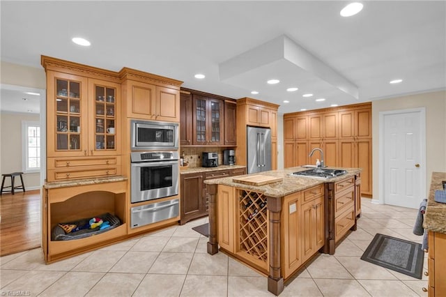 kitchen with a kitchen island with sink, stainless steel appliances, light stone countertops, and light tile patterned floors