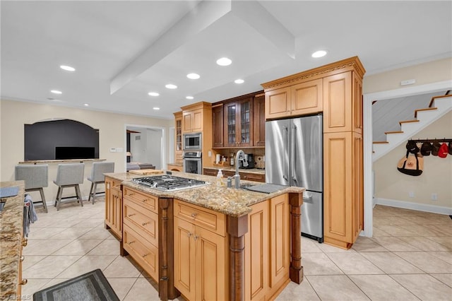 kitchen with an island with sink, stainless steel appliances, sink, light stone countertops, and light tile patterned floors