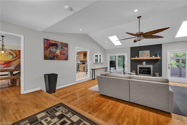 living room featuring vaulted ceiling with skylight, light hardwood / wood-style flooring, a fireplace, and plenty of natural light