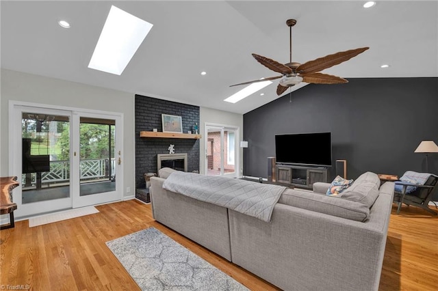 living room featuring light hardwood / wood-style flooring, ceiling fan, a brick fireplace, and vaulted ceiling