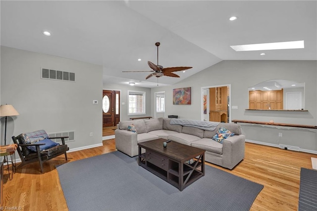 living room with ceiling fan, vaulted ceiling with skylight, and light hardwood / wood-style flooring