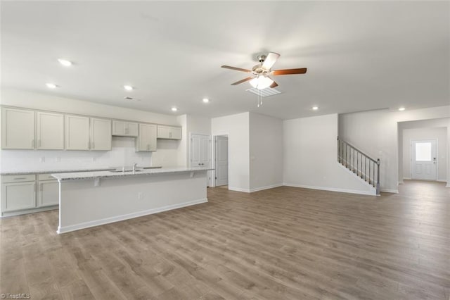 kitchen featuring sink, ceiling fan, light stone counters, a center island with sink, and light hardwood / wood-style flooring