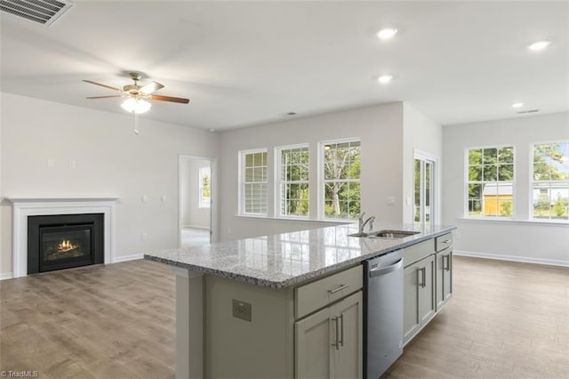 kitchen featuring dishwasher, sink, gray cabinetry, light stone counters, and a center island with sink