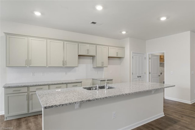 kitchen featuring dark hardwood / wood-style floors, an island with sink, sink, and light stone counters