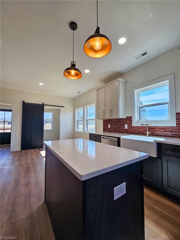 kitchen featuring a barn door, white cabinets, a kitchen island, light countertops, and pendant lighting