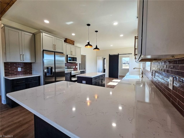 kitchen with decorative light fixtures, stainless steel appliances, a barn door, a kitchen island, and light stone countertops