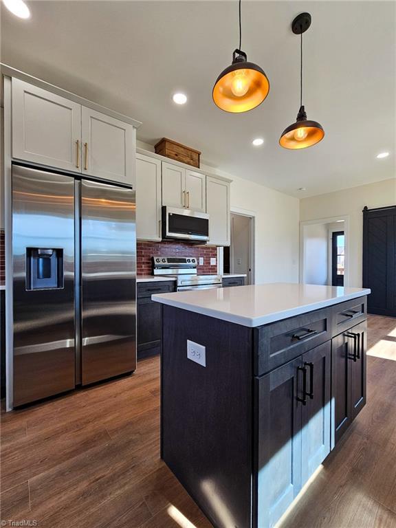 kitchen with stainless steel appliances, light countertops, hanging light fixtures, white cabinetry, and a kitchen island