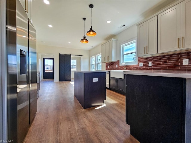 kitchen featuring a barn door, stainless steel fridge with ice dispenser, light countertops, hanging light fixtures, and a center island