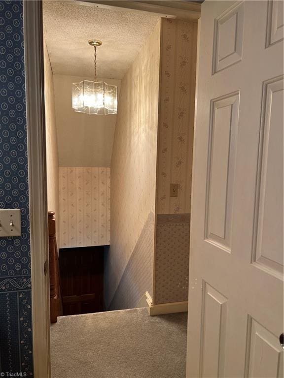 hallway featuring a textured ceiling, carpet, and a chandelier