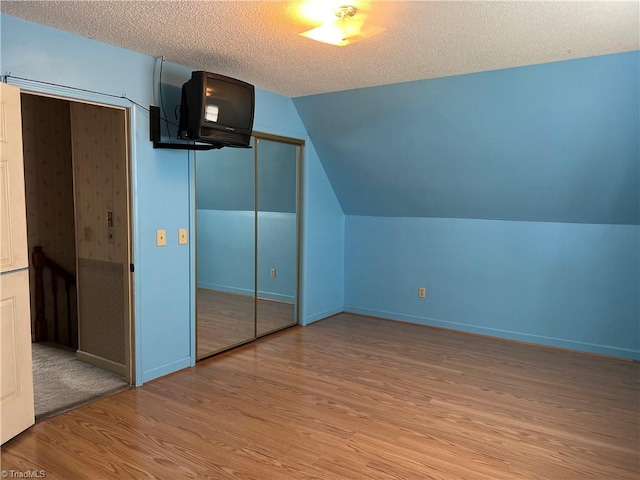 unfurnished bedroom with a textured ceiling, light wood-type flooring, vaulted ceiling, and a closet