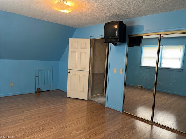 unfurnished bedroom featuring a textured ceiling, lofted ceiling, a closet, and hardwood / wood-style flooring