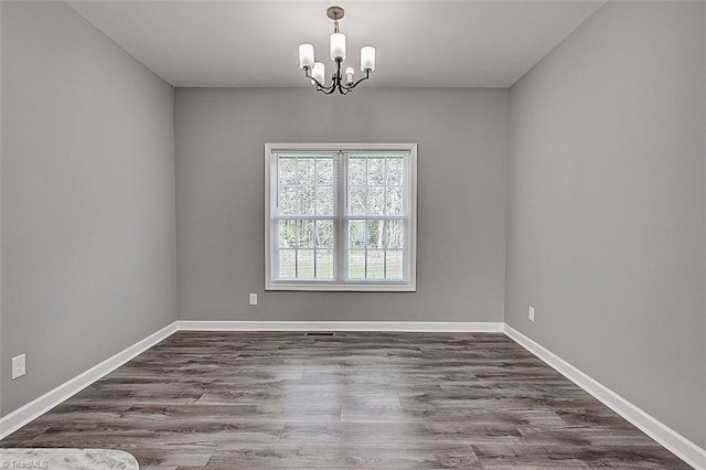 spare room featuring wood finished floors, a notable chandelier, and baseboards