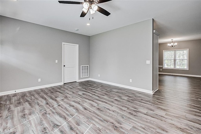 spare room featuring ceiling fan with notable chandelier, wood finished floors, and baseboards