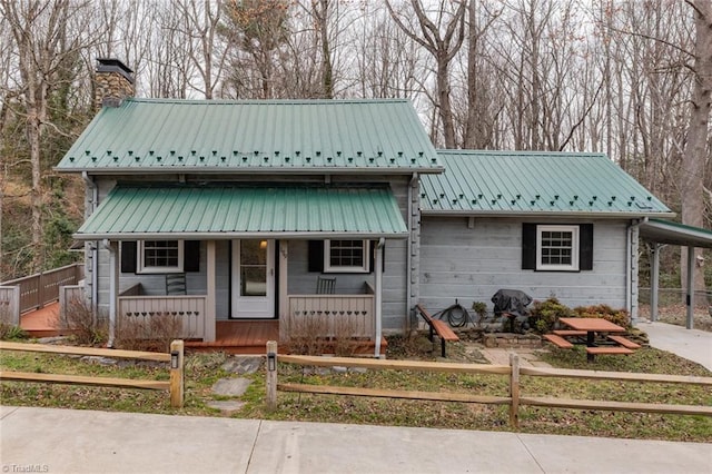 view of front of property with a fenced front yard, covered porch, a chimney, metal roof, and a carport