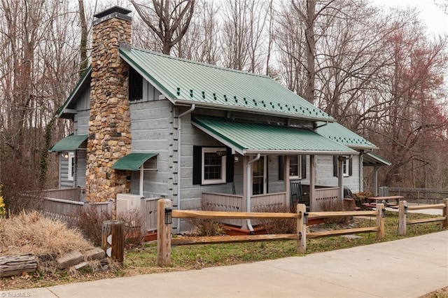 rustic home with a fenced front yard, covered porch, metal roof, and a chimney