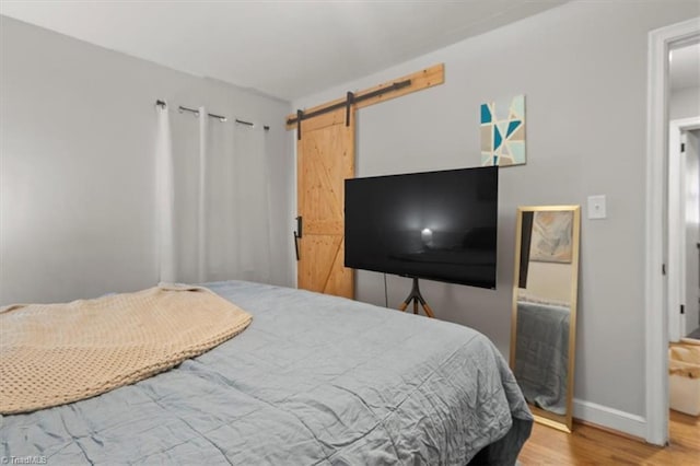 bedroom with a barn door, wood finished floors, and baseboards