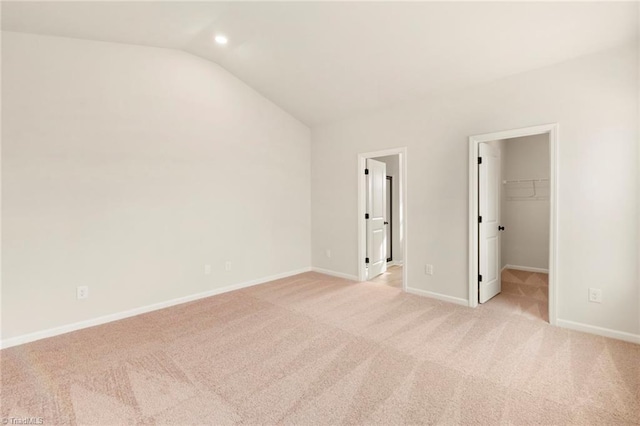 unfurnished bedroom featuring a walk in closet, light colored carpet, vaulted ceiling, and a closet