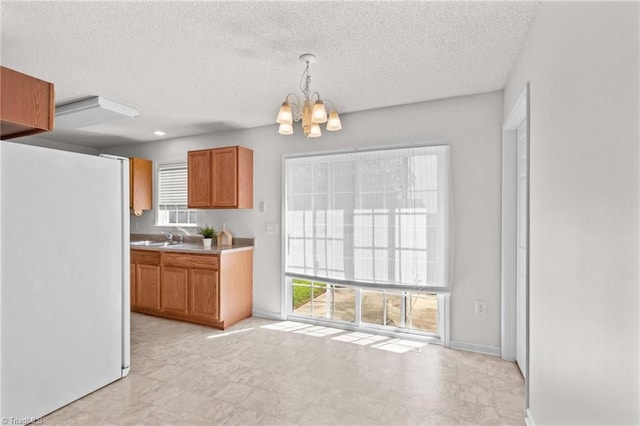 189 Lochshire Ln, Woodleaf, NC 27054 - kitchen with white fridge, a chandelier, a textured ceiling, brown cabinetry, and light countertops