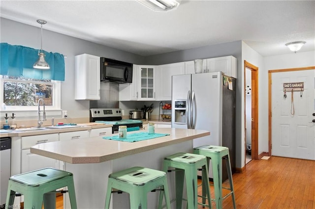 kitchen with black microwave, electric range, a sink, white cabinets, and a kitchen bar