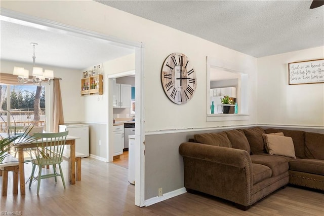 living area featuring baseboards, a textured ceiling, an inviting chandelier, and wood finished floors