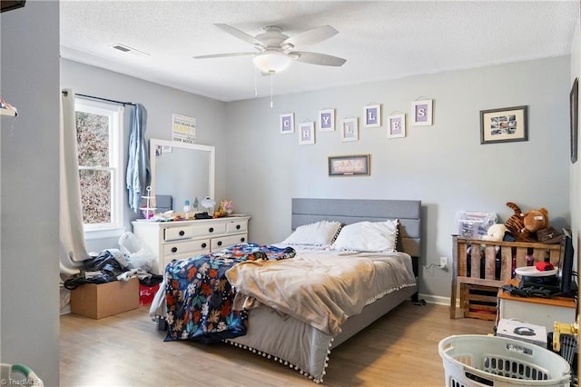 bedroom featuring a ceiling fan, visible vents, a textured ceiling, and wood finished floors