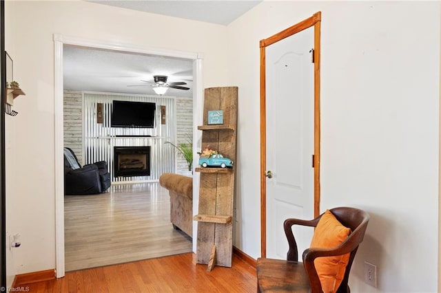 living area featuring light wood-type flooring, a fireplace, a ceiling fan, and baseboards