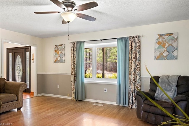 living area with a textured ceiling, ceiling fan, wood finished floors, visible vents, and baseboards