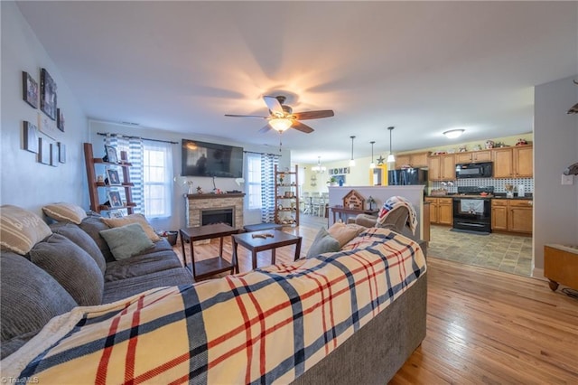 living room featuring ceiling fan, a stone fireplace, and light hardwood / wood-style flooring