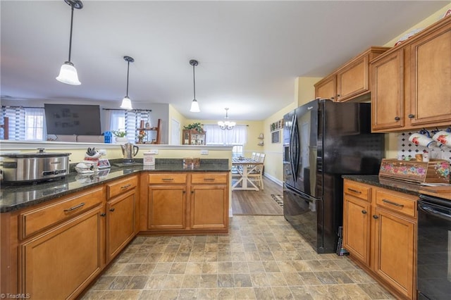 kitchen with dark stone counters, black fridge with ice dispenser, an inviting chandelier, range, and hanging light fixtures