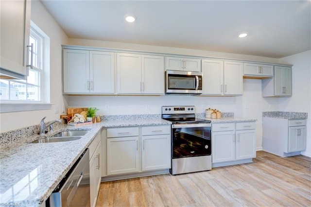 kitchen featuring appliances with stainless steel finishes, sink, light stone counters, and light hardwood / wood-style flooring