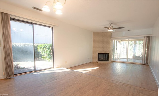 unfurnished living room with ceiling fan with notable chandelier, a brick fireplace, and light wood-type flooring