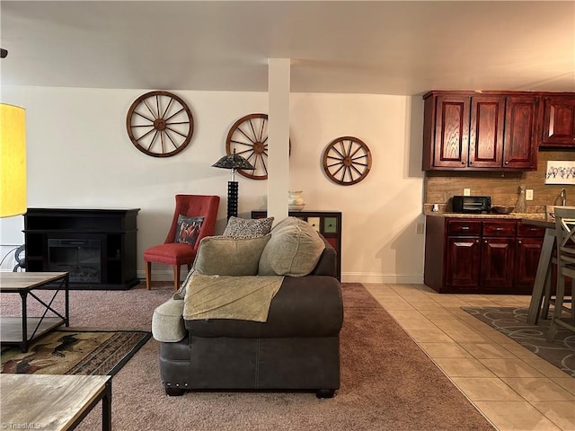 living area with light tile patterned flooring, a glass covered fireplace, and baseboards