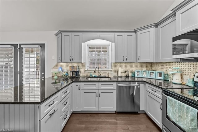 kitchen featuring stainless steel appliances, a peninsula, a sink, dark wood-style floors, and dark stone countertops