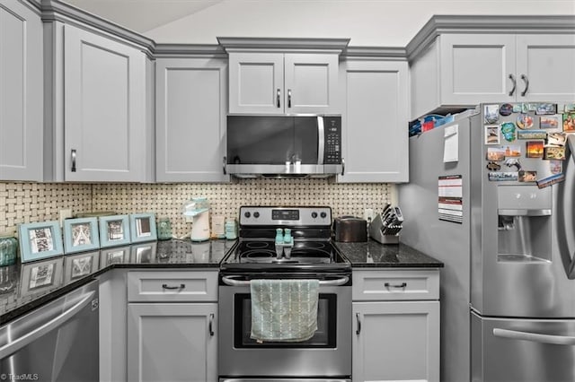 kitchen with tasteful backsplash, lofted ceiling, gray cabinetry, appliances with stainless steel finishes, and dark stone countertops