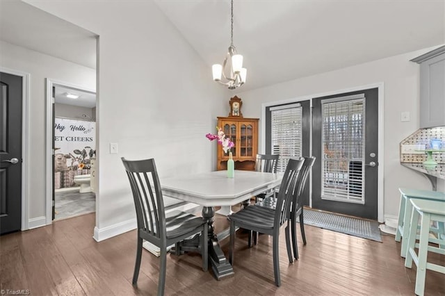 dining room featuring dark wood-type flooring, a notable chandelier, vaulted ceiling, and baseboards