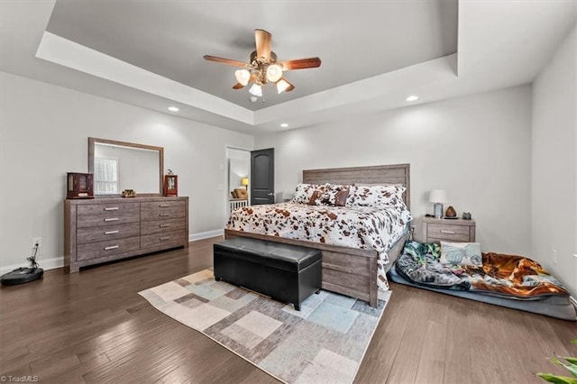 bedroom featuring ceiling fan, a tray ceiling, wood finished floors, and baseboards