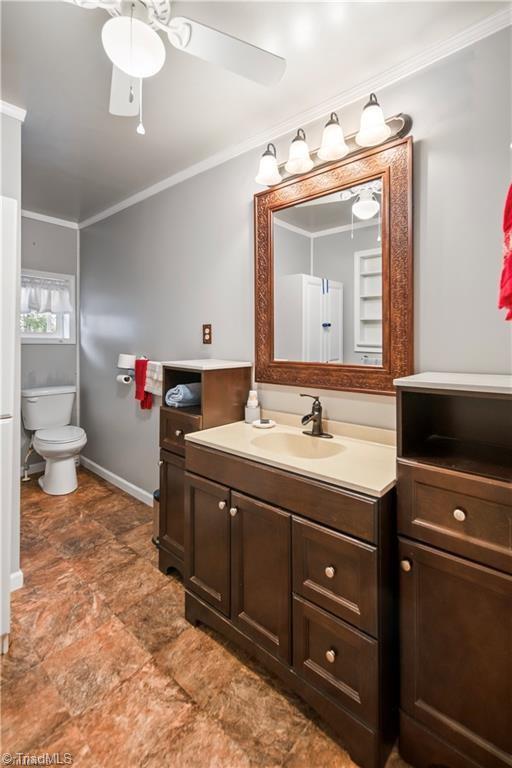 bathroom featuring ceiling fan, toilet, vanity, baseboards, and ornamental molding