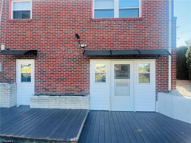 entrance to property featuring brick siding and a deck