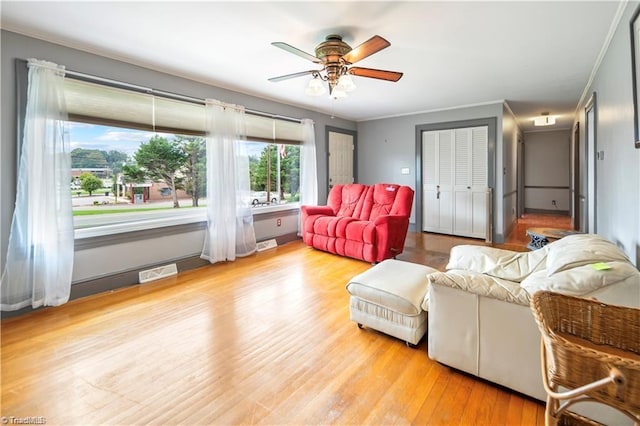 living room with ornamental molding, visible vents, ceiling fan, and wood finished floors